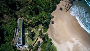 An aerial view of a beachside property with a long building, surrounded by dense greenery and a sandy beach. - Modern Beach Villa With Roof Garden (Talalla)