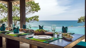 A dining table set with plates, glasses, and cutlery, overlooking a beach with the ocean and trees. - Spectacular Hilltop Beach Villa Located Next To A Surf Break (Nilwella)
