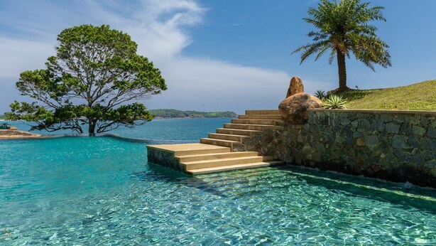 A clear pool with steps leading to a stone wall, surrounded by trees and a view of the sea. - Spectacular Hilltop Beach Villa Located Next To A Surf Break (Nilwella)