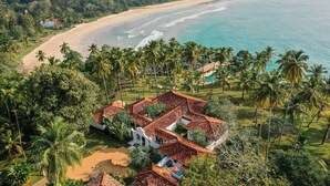 An aerial view of a coastal property with a beach, palm trees, and a white building with a red roof. - Spectacular Hilltop Beach Villa Located Next To A Surf Break (Nilwella)