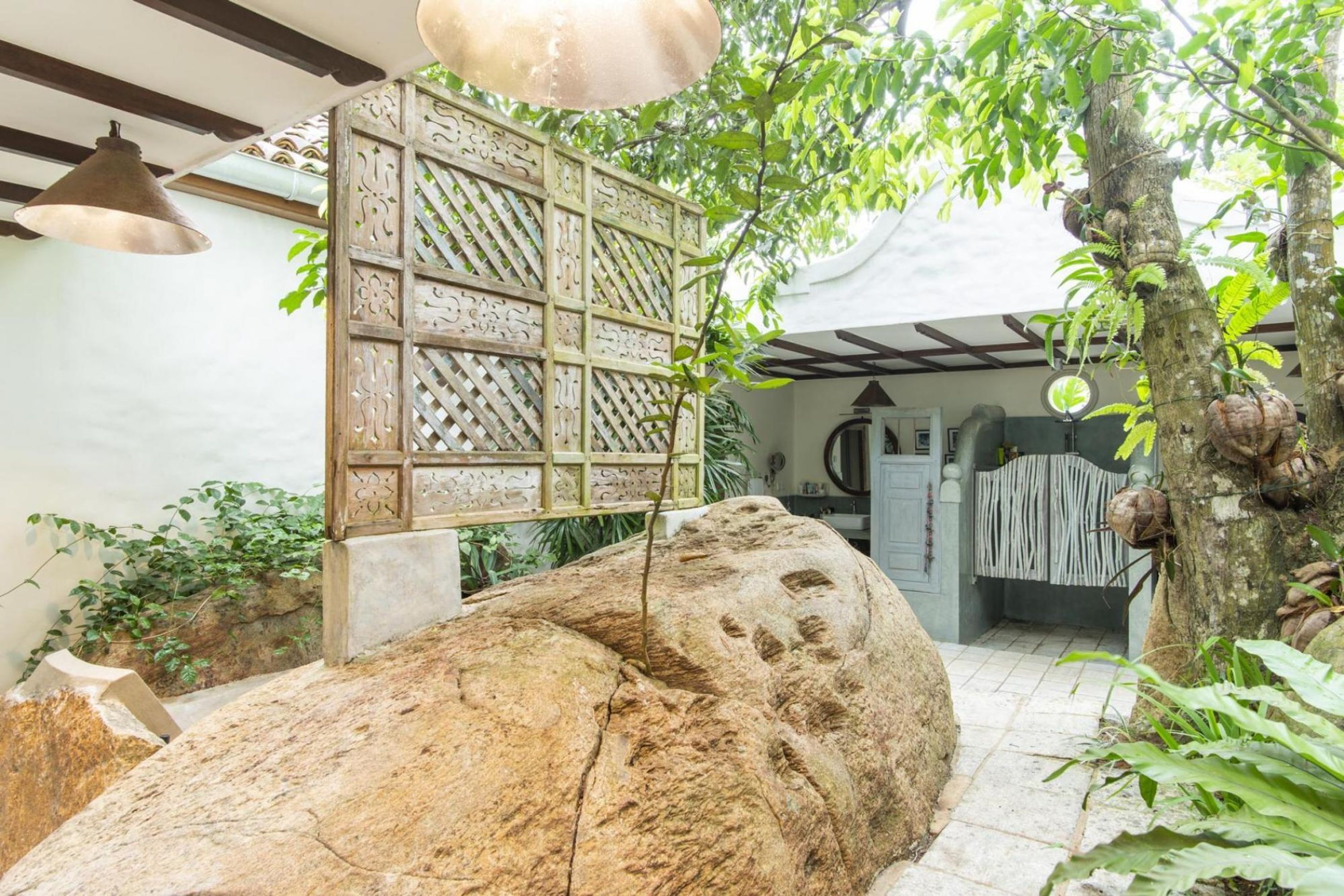 A stone pathway leading to a room with a large rock, a decorative lattice wall, and a hanging light fixture.