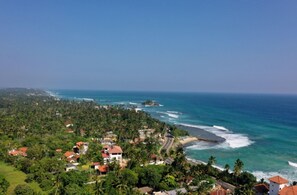 A coastal area with houses surrounded by dense greenery, a beach, and the ocean. - Beautifully Renovated Family Village House Within Walking Distance To The Beach (Ahangama)