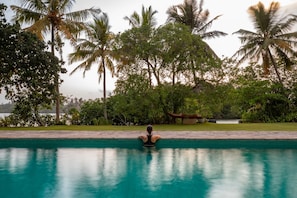 A person relaxing in a swimming pool with a view of palm trees and a body of water in the background. - Lovely Lakeside Villa With Large Pool Poolside Dining (Koggala)