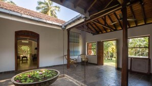 A spacious indoor area with a stone water feature, wooden furniture, and large windows allowing natural light. - Refurbished Family Village House With Private Pool (Koggala)
