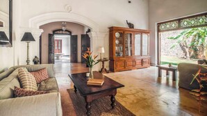 A spacious living room with a large wooden cabinet, a sofa, a coffee table, and a view of a garden through a window. - Refurbished Family Village House With Private Pool (Koggala)