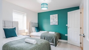 A bedroom with two beds, a teal accent wall, a white door, and a ceiling light fixture. - tms Cheerful 5bdr House! Thurrock! Free Parking! (Stanford-le-Hope)
