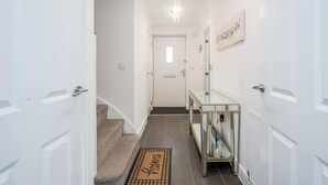 A hallway with a carpeted staircase, a glass console table, and a door at the end. - tms Cheerful 5bdr House! Thurrock! Free Parking! (Stanford-le-Hope)