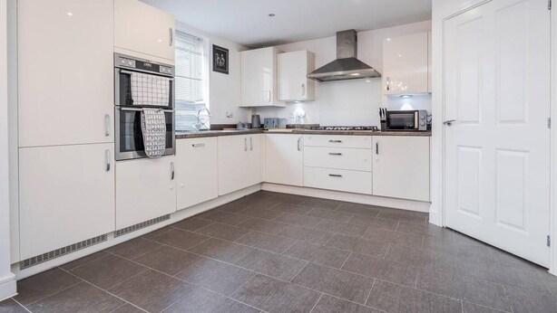 A modern kitchen with white cabinets, a stainless steel range hood, and a microwave. - tms Cheerful 5bdr House! Thurrock! Free Parking! (Stanford-le-Hope)