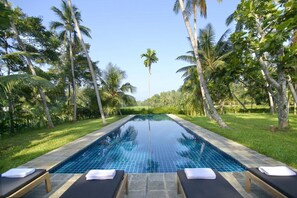 A rectangular infinity pool with clear blue water, surrounded by lush greenery and palm trees.