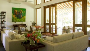 A spacious living area with a beige sofa, a coffee table with a vase of flowers, and a painting on the wall. - Family House With Large Garden In A Peaceful Setting (Padinnoruwa)