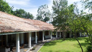 A building with a tiled roof, covered patio area with chairs and tables, and a well-maintained lawn. - Family House With Large Garden In A Peaceful Setting (Padinnoruwa)