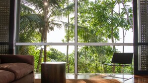 A modern living room with a large window, a brown sofa, a round wooden table, and a black chair. - Historically Important Architecturally Stunning Hilltop Villa (Hapugala)
