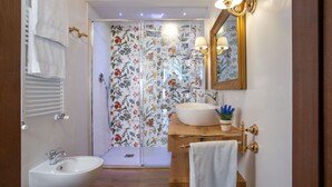 Ein Badezimmer mit einem weißen Waschbecken, einem spiegel mit goldener Rahmen und einer Dusche mit floralem Wandpapier.