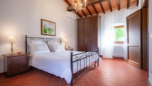 Ein Schlafzimmer mit einem Bett, Nachttischen, einer Deckenleuchte, einem großen Kleiderschrank und einem Fenster mit Vorhängen.