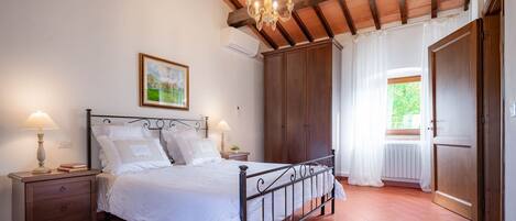 A bedroom with a bed, nightstands, a chandelier, a large wardrobe, and a window with curtains.