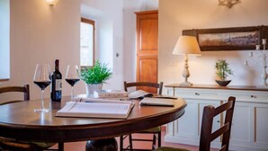 A dining area with a round wooden table, two wine glasses, a bottle of wine, a book, and a lamp. - Iris apartment (Città metropolitana di Firenze)