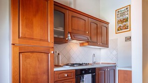 A kitchen with wooden cabinets, a gas stove, an oven, and a tiled backsplash. - Iris apartment (Città metropolitana di Firenze)