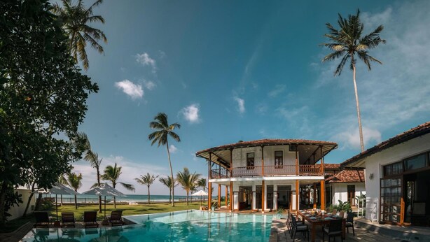 A poolside area with a two-story building, palm trees, and a view of the ocean. - Family Beach Villa Located On An Incredible Beach (Koggala)