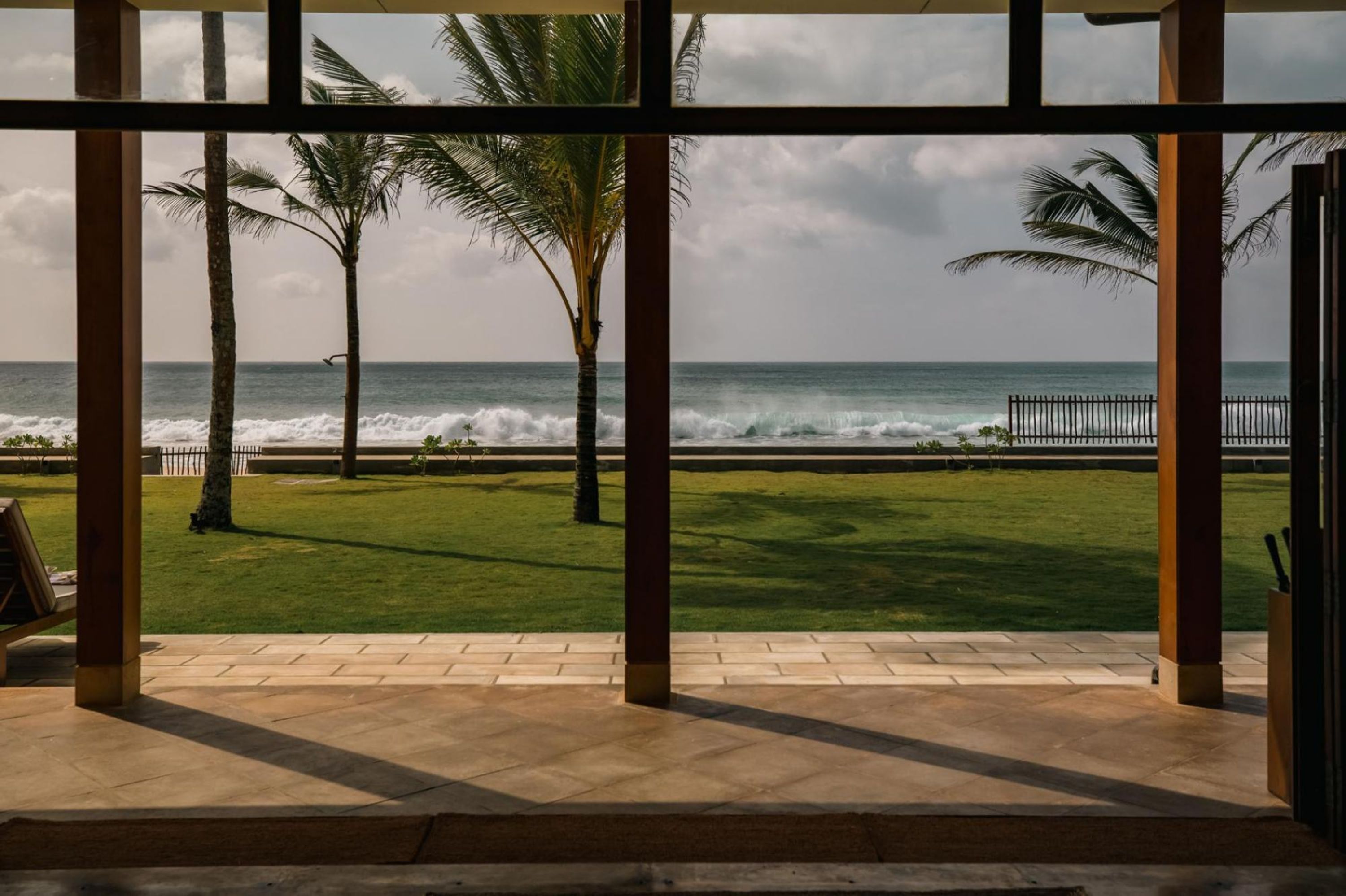 A view from inside a building with large windows overlooking a beach with palm trees and waves.
