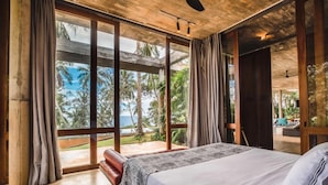 A bedroom with a large bed, wooden ceiling, and a view of palm trees and a pool. - Sustainably Designed Villa Overlooking Indian Ocean (Tangalle)