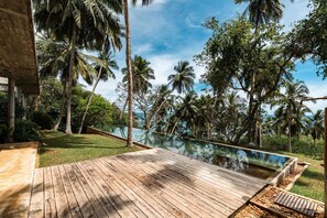 A wooden deck with a pool, surrounded by palm trees and a clear sky.