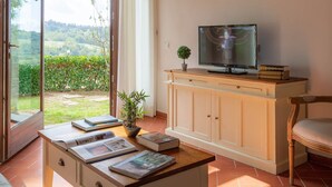 A cozy living room with a wooden ceiling, a television on a cabinet, a sofa, and a table with books and a plant. - Primula apartment (Città metropolitana di Firenze)