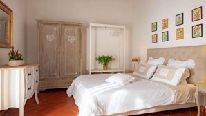 A bedroom with a large bed, a dresser, a wardrobe, a bedside table with a lamp, and a wall with framed pictures. - Primula apartment (Città metropolitana di Firenze)