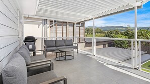 Un espace de vie extérieur moderne, avec un canapé gris, une table ronde et un barbecue.