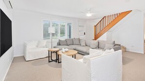 Un salon moderne avec un canapé d’angle, un fauteuil blanc, une table basse et un escalier doté de rampes en bois.