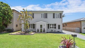 Une maison à deux étages avec un porche à l’avant, une pelouse bien entretenue et un petit jardin agrémenté d’un palmier.