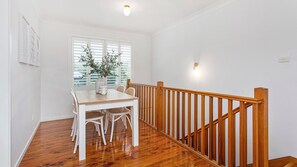 Un coin repas avec une table et des chaises en bois, un vase agrémenté de verdure et un escalier avec des rampes en bois.