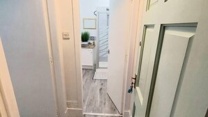 A hallway with a wooden floor, white walls, and a door leading to a bathroom with a shower. - Granite Getaways - The Terrace Below (Aberdeen)