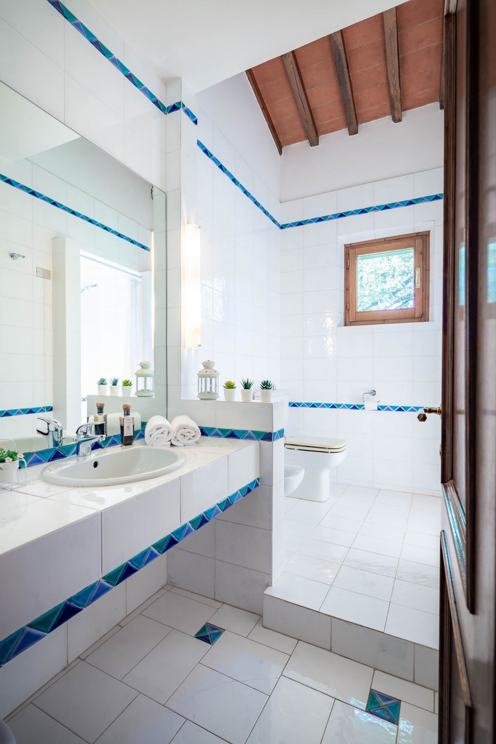 Ein modernes Badezimmer mit einem großen Spiegel, zwei Waschbecken, einer Toilette und einem Fenster.