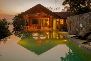 Una villa moderna con piscina, mobiliario exterior y un muro de piedra.