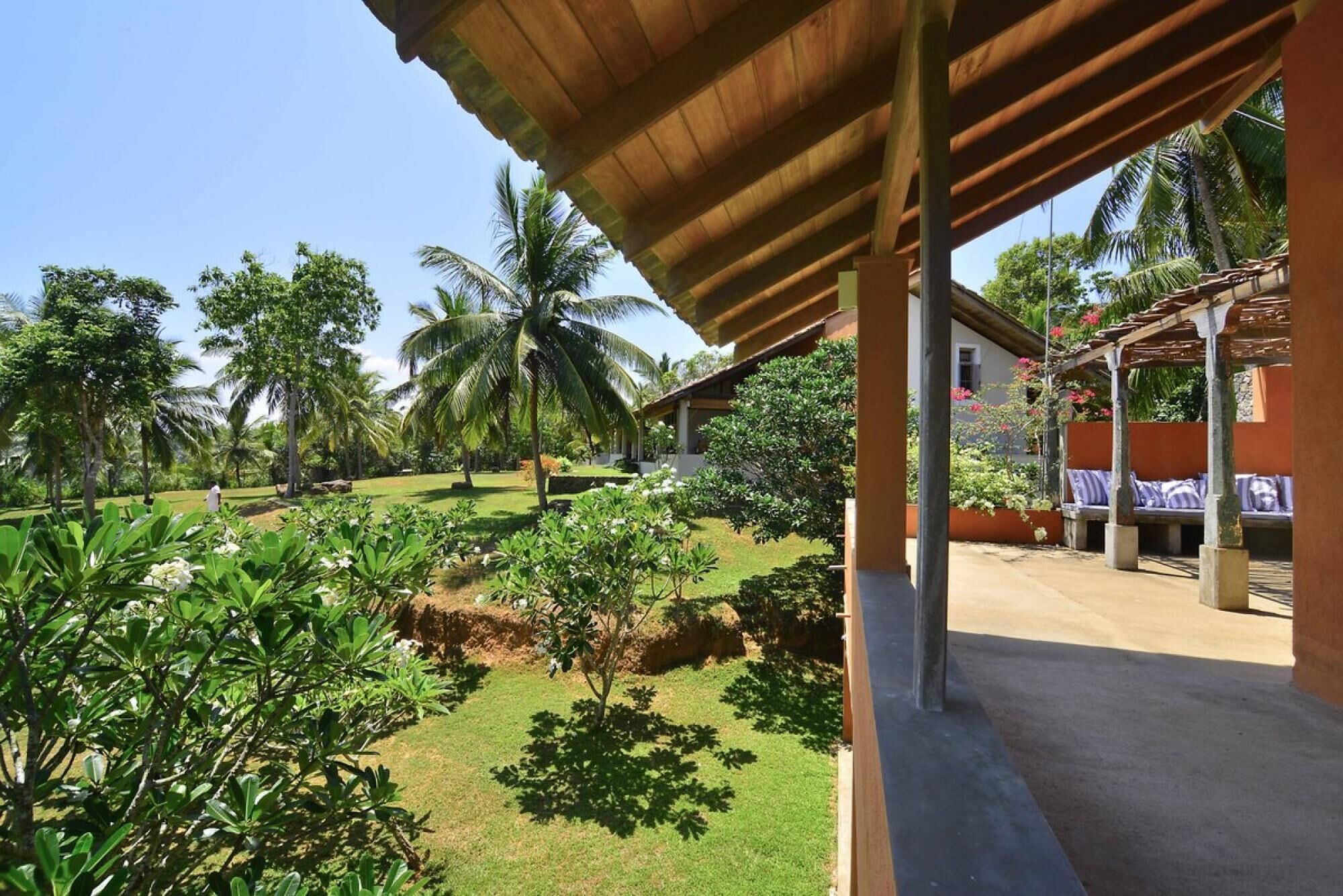 A covered outdoor area with a concrete floor, surrounded by lush greenery and palm trees.