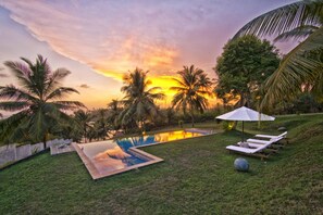 A pool area with lounge chairs and an umbrella, surrounded by palm trees and a sunset view. - Elevated Family Beach House With Ocean Views (Dikwella)