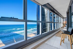 A modern hotel room with large windows overlooking the ocean and a cityscape.