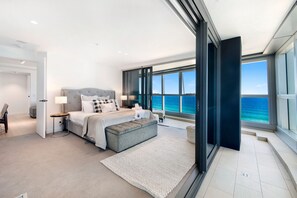 A modern bedroom with a large bed, a view of the ocean, and a sliding glass door leading to a balcony.