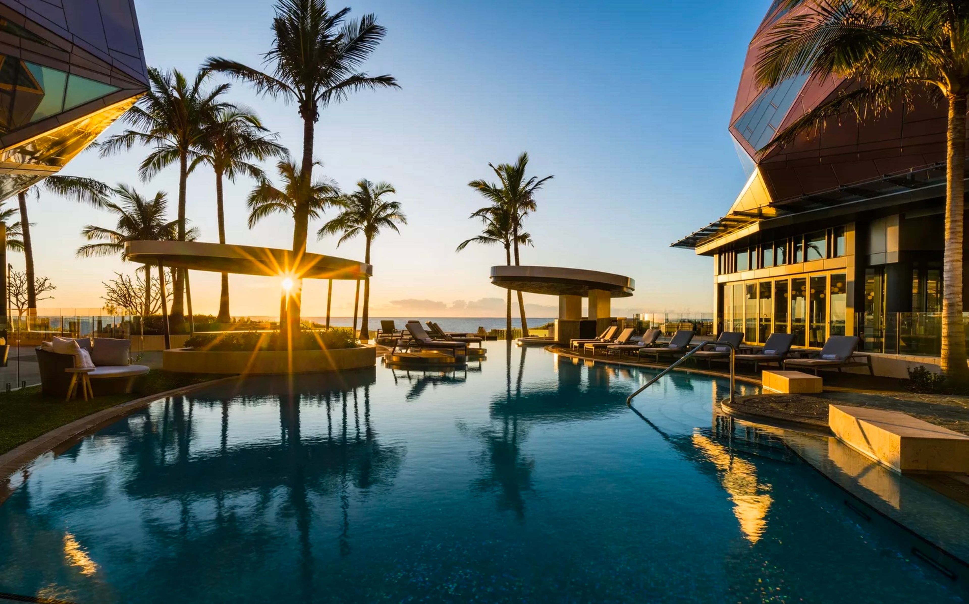 A pool area with lounge chairs and palm trees, surrounded by modern architecture.