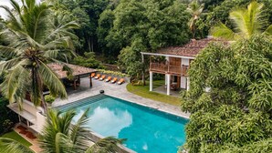 A pool with lounge chairs, surrounded by lush greenery and a two-story building with a balcony. - Luxurious 07 Bedroom Hilltop Villa With Private Gym (Unawatuna)