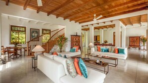 A spacious living area with a high ceiling, wooden beams, a white sofa with colorful cushions, a dining area with wooden furniture, and a staircase leading to another level. - Luxurious 07 Bedroom Hilltop Villa With Private Gym (Unawatuna)