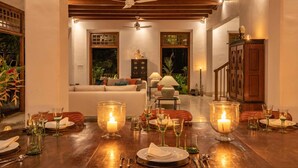 A dining area with a wooden table set for a meal, candles, and a view of a living room with a sofa and a ceiling fan. - Luxurious 07 Bedroom Hilltop Villa With Private Gym (Unawatuna)