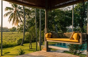 A wooden swing chair with cushions, a pool, and a view of a green landscape with trees. - Antique Dutch Period Country House With Far Reaching West-facing Views (Unawatuna)