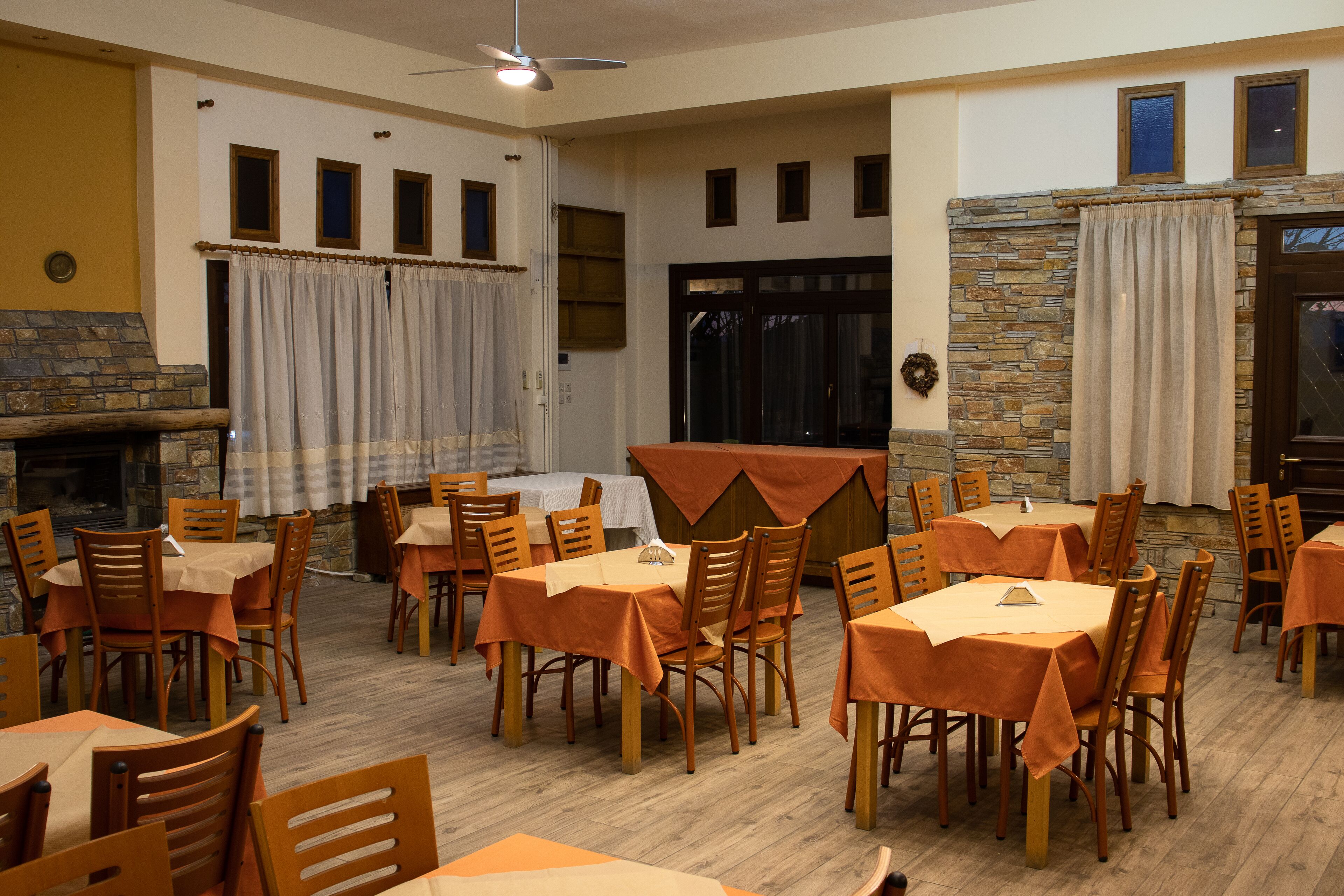 A dining area with multiple tables and chairs, a stone fireplace, and a view of the outdoors through a door.