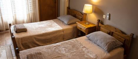 A hotel room with two single beds, a wooden headboard, a bedside table with a lamp, and a radiator.