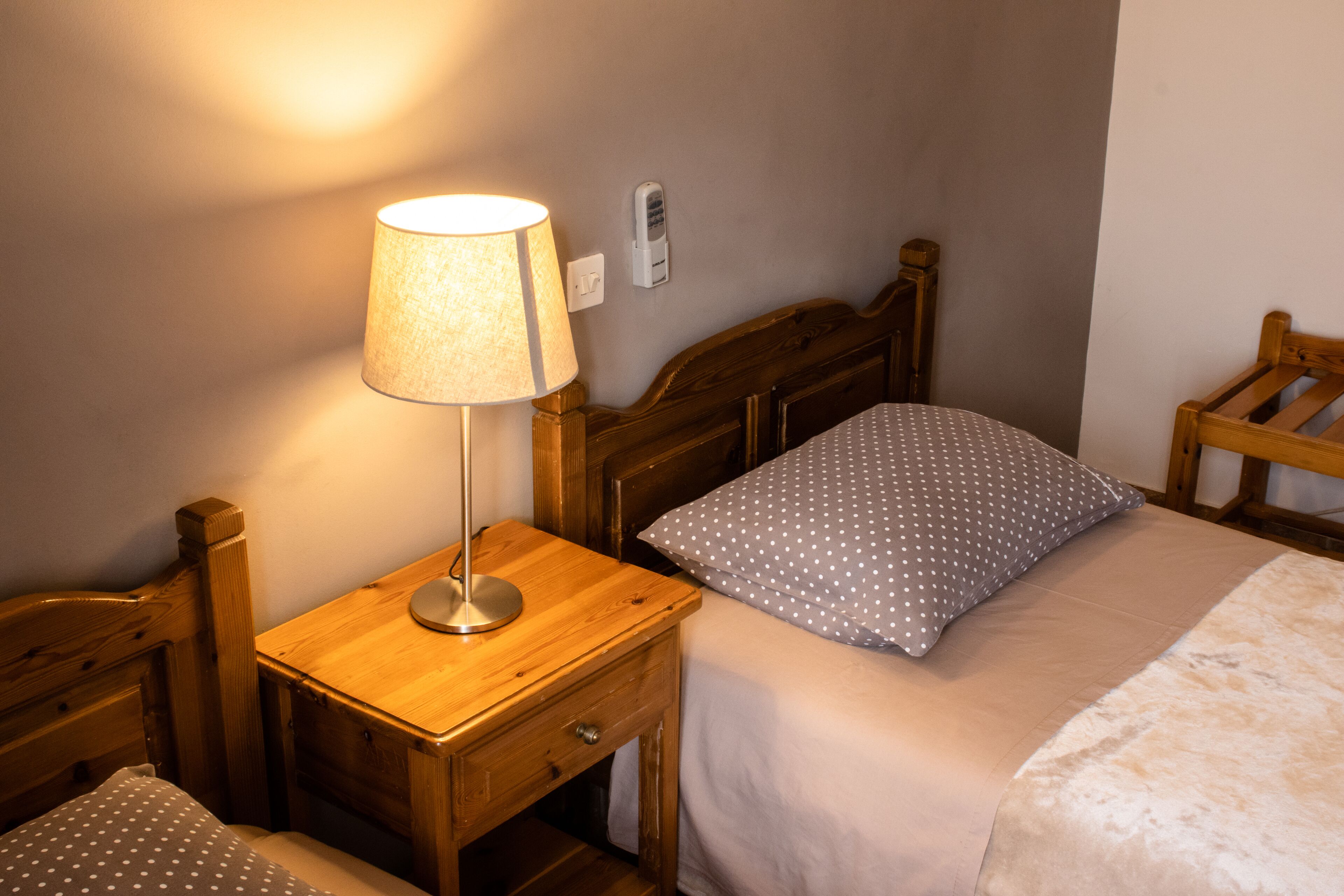 A wooden bed with a white and gray polka dot pillow, a wooden nightstand with a lamp, and a wooden chair.