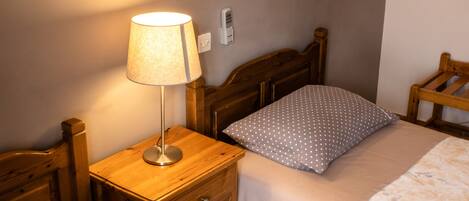 A wooden bed with a white and gray polka dot pillow, a wooden nightstand with a lamp, and a wooden chair.