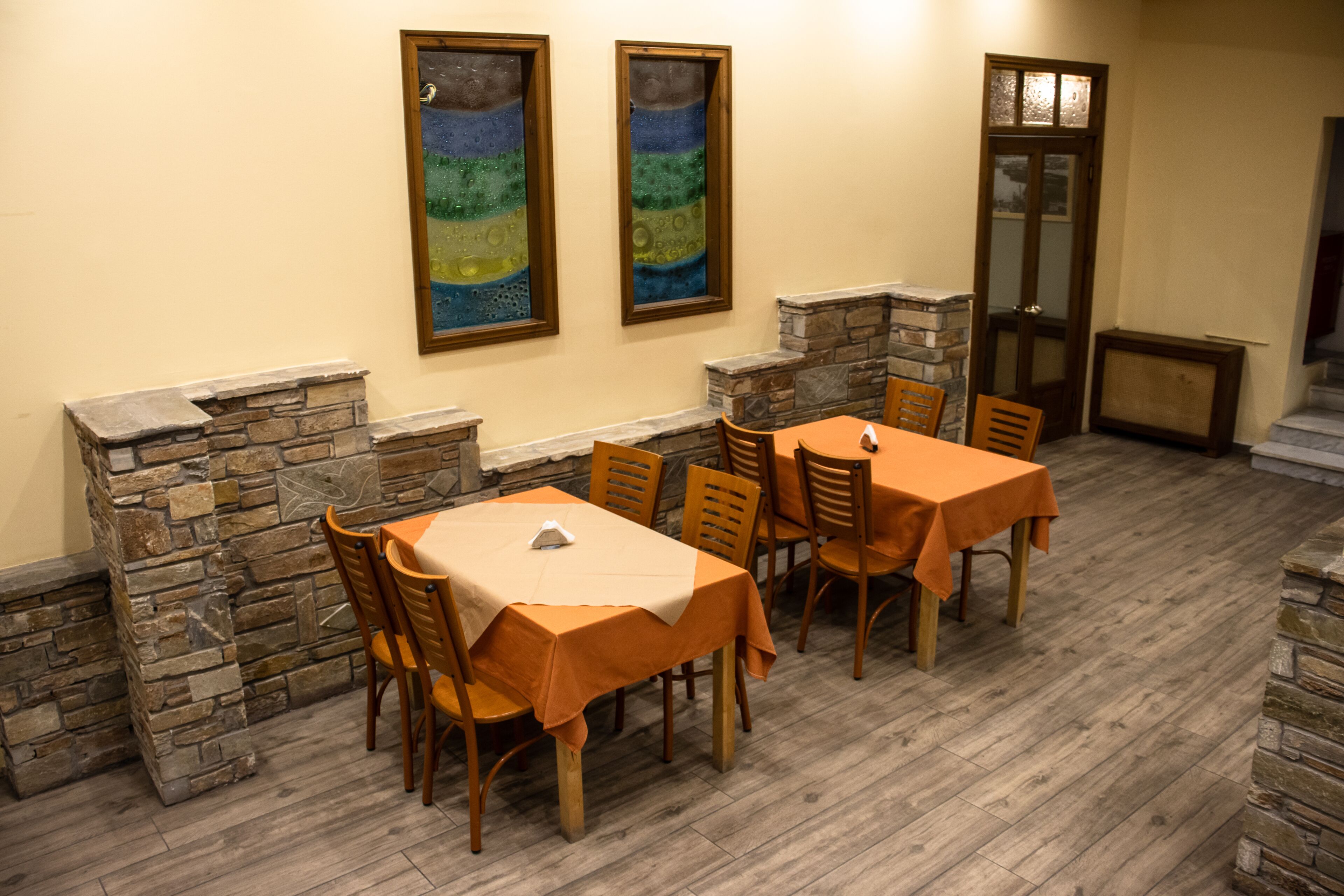 A dining area with stone walls, wooden chairs, and tables covered with orange tablecloths.