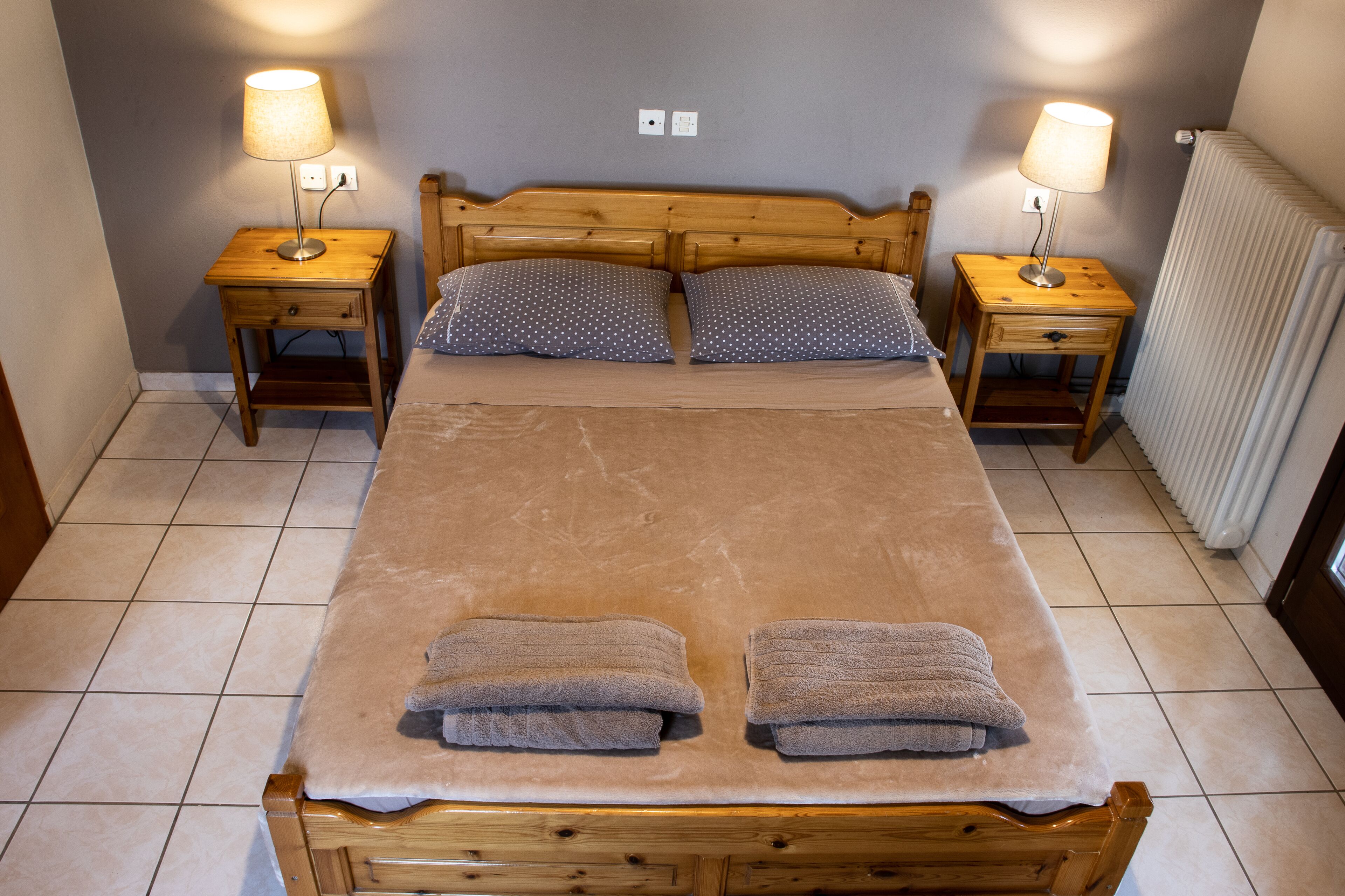Una cama doble con cabecera de madera, dos mesitas de noche con lámparas, dos almohadas y dos toallas sobre la cama.