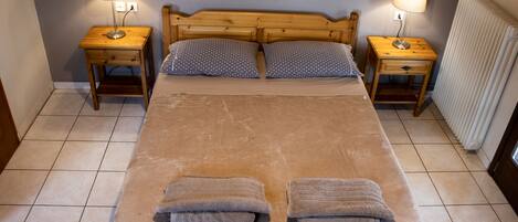 A double bed with a wooden headboard, two bedside tables with lamps, two pillows, and two towels on the bed.